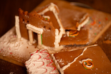 Horizontal photo. Broken tasty brown gingerbread house with white powdered sugar, icing decor on wood cut board on table. Top view. Concept of sweet food, repair, Merry Christmas gift, Happy New Year