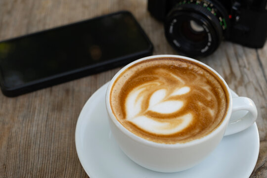 Creative workspace with coffee, camera, and phone. Latte coffee with camera and smartphone on wooden table. Coffee break with camera and mobile phone. - Powered by Adobe