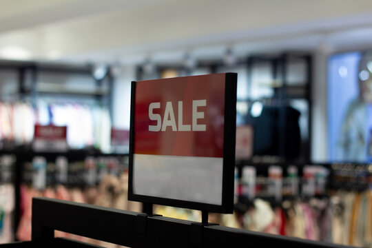 Horizontal defocused photo. Selective focus. Board with red text Sale in clothing store interior. Concept of online shopping, Black Friday, cyber monday, mega discount, 11 november, gift, offer