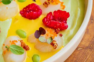 A colorful dessert showcases lychee, raspberries, and mango puree with artistic garnishes