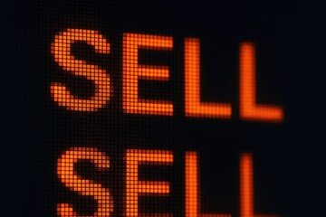 Digital board displays the word sell in orange LED lights with stock market sell signals