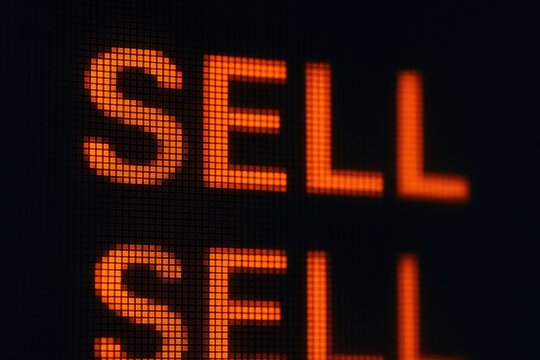 Digital board displays the word sell in orange LED lights with stock market sell signals