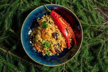 A vibrant plate of aromatic rice, topped with a red chili and herbs, among pine branches