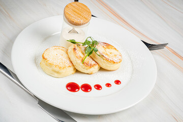 Three fluffy pancakes topped with powdered sugar, berry sauce, and fresh cream