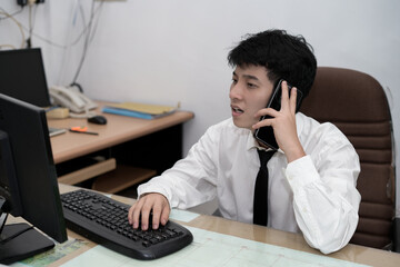 A young Asian professional or businessman sitting at his desk, engaged in a serious or thoughtful conversation on a telephone in a office environment