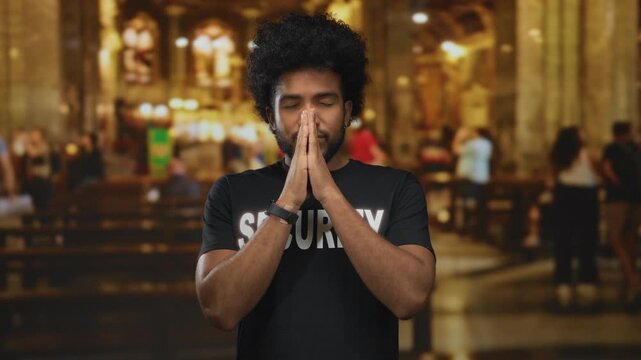 Man wearing security uniform with eyes closed in prayer inside church with blurred interior background offering a serene and reflective atmosphere.