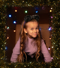 Happy child wearing mouse ears in a festive gift box with Christmas lights and tinsel, purple sweater, playful mood