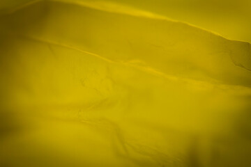 Extreme close up of yellow empty plastic bag background. The plastic surface is wrinkly and tattered making abstract pattern. Selective focus, shallow depth of field.