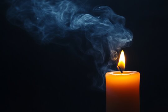 Close up of a burning orange candle with wisps of blue smoke rising against a dark background