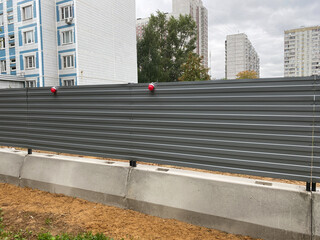 Metal hoarding. Construction steel fence with red markers and concrete base. Perimeter corrugated fence.