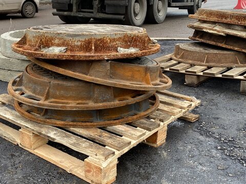 Stack of rusty metal manhole covers on wooden pallet outdoors. Road repair, dismantling of old manholes, replacement of utilities.