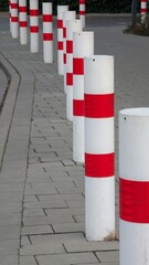 Red and white bollards in city. A series of red and white bollards line the sidewalk in an urban area, creating a clear barrier. The setting appears orderly and well-maintained.