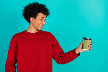 Young man in a red sweater smiles while holding a takeout coffee cup against a teal background for lifestyle and fashion stock