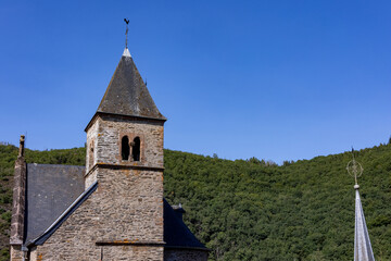 Esch-sur-Sure, Wiltz, Grand-Duche de Luxembourg, September 07, 2025, Skyline with spire, Quiet scene showing historic church spire beneath vibrant blue sky with surrounding forested horizon