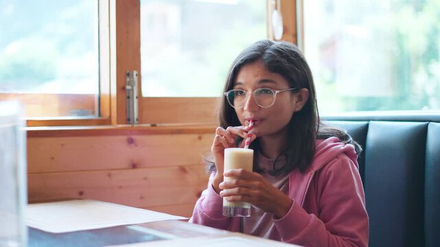 4K shot of young Indian woman drinking cold coffee in cafe. Beautiful woman relaxing and drinking morning cold coffee. Asian female enjoying a cup of coffee