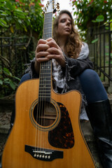 Young woman musician sitting outdoors holding acoustic guitar with abstract blurred background