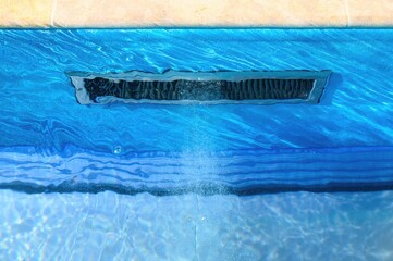 Close-up of a pool skimmer integrated into the side wall, with water actively circulating through...