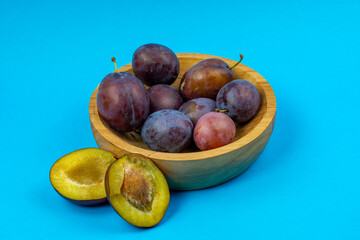 Fresh plums in a wooden bowl with sliced fruits arranged on a solid light blue background in a top-view studio composition