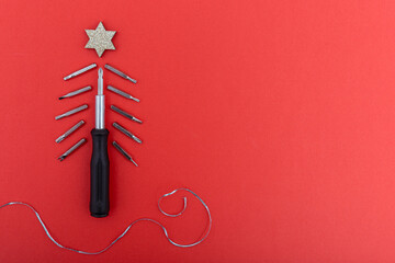 Screwdriver and bits arranged as christmas tree with glitter star on red background. Creative concept of festive spirit and craftsmanship in minimalist style. Copy space