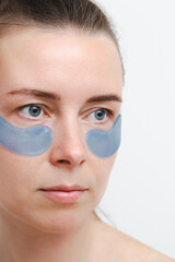 Portrait of a young european girl or woman a blue mask and patches for the skin around the eyes. Vertical photo