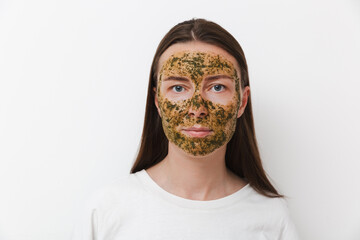 Portrait of young girl or woman with green natural homemade cosmetic mask on her face with white background. Concept of self-care at home or in salon. Copy space