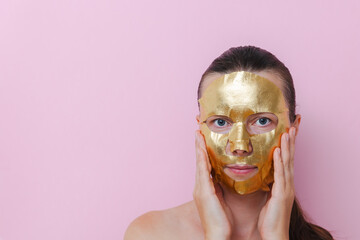Woman applying golden sheet mask and touching cheek. Concept of luxury skincare, rejuvenation and modern beauty self care routine. Copy space