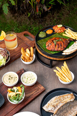 Shot of tandoori pomfret served with fries, salad and chutney, alongside panfried seabass with cocktail and dips, creating a flavorful restaurant-style seafood presentation with vibrant plating.