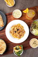 Cheese seafood penne served in a white plate on a wooden board, styled with a creamy dip, fresh salad, crispy fries, and a cocktail, creating a vibrant and appetizing restaurant presentation