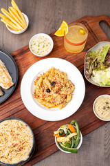 Cheese seafood penne served in a white plate on a wooden board, styled with a creamy dip, fresh salad, crispy fries, and a cocktail, creating a vibrant and appetizing restaurant presentation
