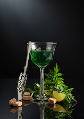 Glass of absinthe with ingredients on a black background.