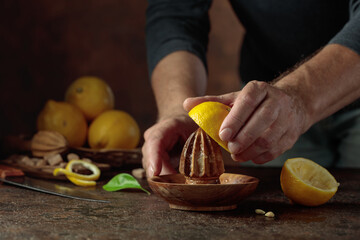 Chef squeezes juice from fresh lemons using an old wooden juicer.