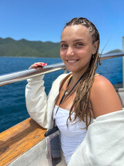 Young woman with braided hair relaxing on a boat, smiling in the warm summer light. Fresh, carefree travel mood on the water with a bright outdoor atmosphere.