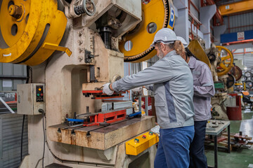 Industrial engineers wearing safety gear inspecting heavy machinery in a modern factory. Factory management, technical maintenance, and engineering teamwork in manufacturing industry.