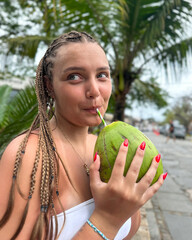 Young woman holding a fresh green coconut in front of lush tropical greenery. Vibrant summer atmosphere, travel lifestyle, exotic vacation mood, nature background.