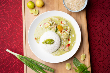 Thai green fish curry served with sticky rice on a wooden board, styled with fresh lemon slices, spring onion and raw rice, creating a vibrant and flavorful Asian food presentation 