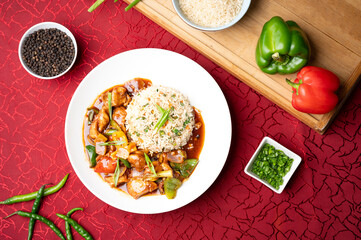 Calcutta chilli chicken with fried rice served on a white plate, styled with sliced capsicums, fresh green chillies, raw rice and black pepper for a vibrant Indo-Chinese food presentation.