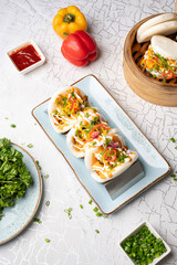 Top view of pulled butter chicken bao with pickled onions and tandoori mayo paired with crispy chilli chicken bao and hot garlic sauce, styled with red chilli sauce, cut green chillies, capsicums