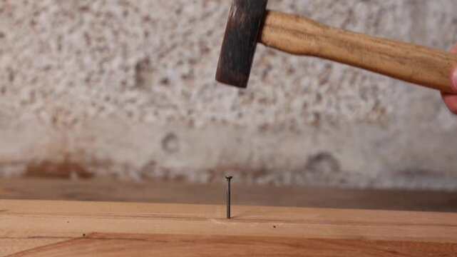 Un marteau en train de taper sur un clou sur une planche de bois dans un atelier.