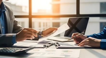 Two business people reviewing documents and using a laptop in a modern office setting with sunlight