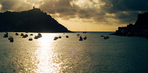 Boote auf ruhigem Meer bei Sonnenuntergang vor dunkler Küstenlandschaft