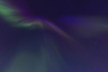 Faint and colorful light of the Northern Lights showing green and violet hues against the dense...