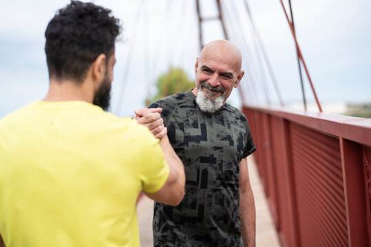 A 65-year-old man and his 40-year-old son warm up, bumping hands to encourage each other and flexing their muscles before going for a run.