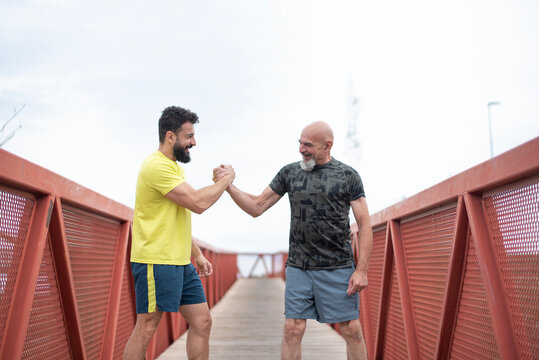 A 65-year-old man and his 40-year-old son warm up, bumping hands to encourage each other and flexing their muscles before going for a run.