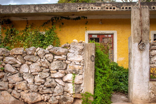 Rustic yellow house in Izamal, Mexico with overgrown vines, old stone wall, weathered doorway, and textured façade capturing authentic Yucatán architecture, rural charm, and traditional colonial villa