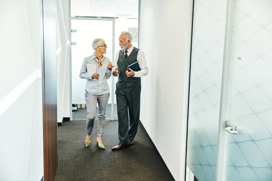 Portrait of two senior businesspeople, elderly business woman and man having a meeting or a break walking in a corridor or standing in the office. - Powered by Adobe
