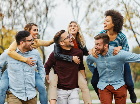 Happy multiracial friends having fun together outdoors in the park. Cheerful young people socializing outdoors. University students laughing together  and running piggyback. Youth culture and friendsh