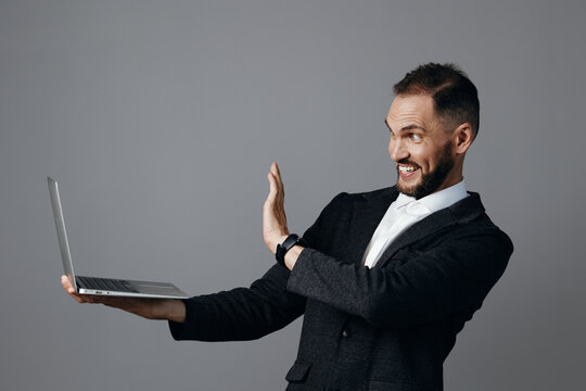 A professional man in a business suit holds a laptop, smiling and gesturing in triumph against a solid colored backdrop, conveying confidence, focus, and dynamic energy.
