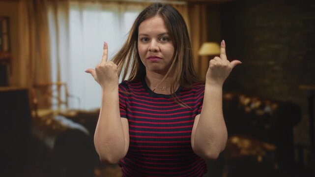 Woman raising both middle fingers inside a hotel building, facing camera with striped shirt and visible fingers and forearms, closeup frontal pose; defiance.