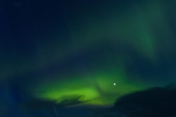 Bright, dynamic green swirls of the Northern Lights fill the dark night sky, with a prominent star visible in the middle of the celestial phenomenon