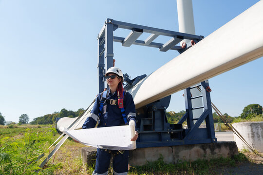 Engineers in safety gear conduct a detailed inspection of wind turbine blades at a construction site. Large blades are placed on the ground, highlighting the renewable energy technology.